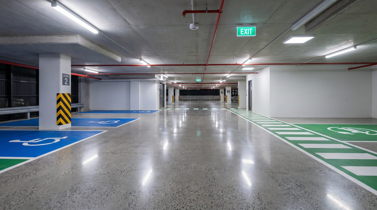 Parlak beton otopark zemininde mavi engelli, yeşil şarj ve bantlı yaya yolu işaretlemeleri; kat kodlu kolon net görünüyor.